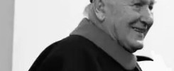 Czarno-białe ujęcie starszego mężczyzny w todze akademickiej, z biretem na głowie. Uśmiechnięty, w okryciu z kołnierzem.