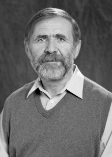 Portret mężczyzny w kamizelce i koszuli. Tło ciemne, jednolite.