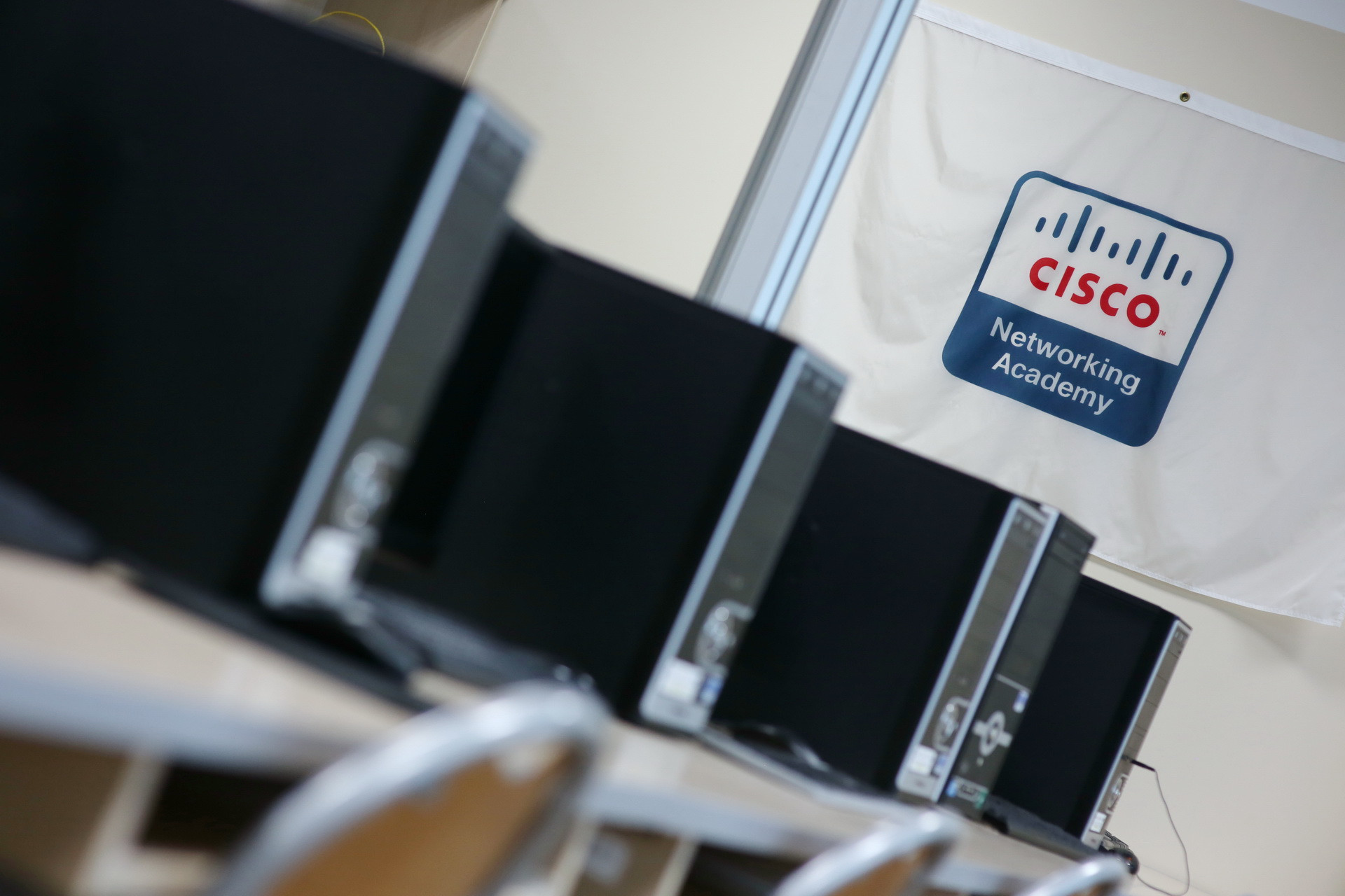 Rząd komputerów z logo Cisco Networking Academy. Kontekst: sala komputerowa.